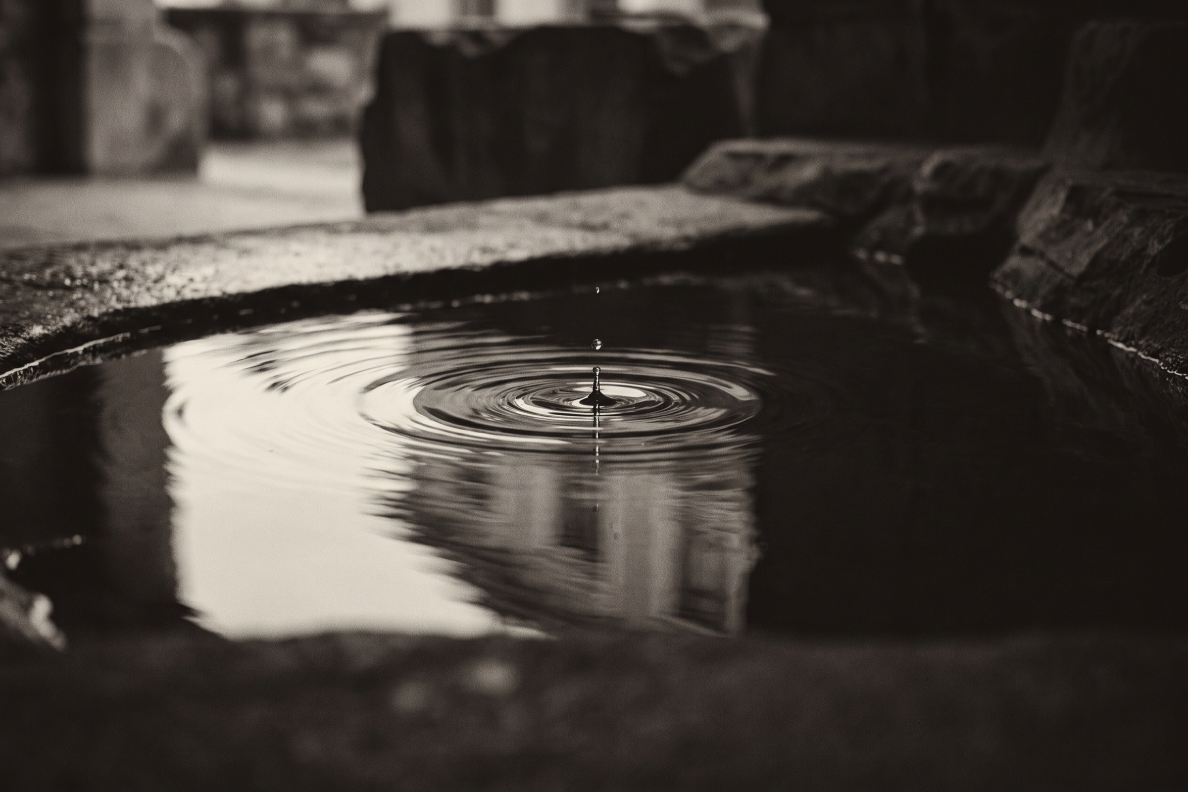 Concentric rings spreading across dark still water where drops have fallen.